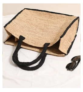 Top view of square raffia tote bag with black trim and handles on white fabric
