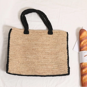 Large raffia woven tote bag with black trim on white fabric with picnic props