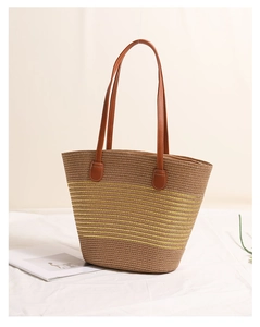 Detail of woven straw tote bag with yellow stripes and brown leather handles on fabric background
