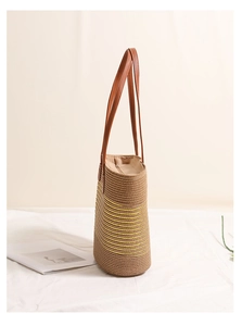 Detail of a brown straw tote bag featuring yellow wave patterns and leather handles
