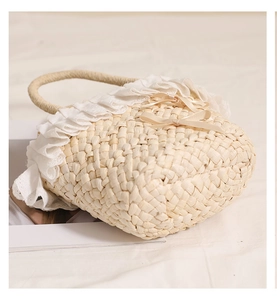 Close-up of handmade straw bag with delicate white lace trim and ribbon bow details