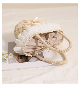 Detailed close-up of straw beach bag with white lace trim and satin bow decoration
