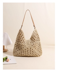 Detail of hollow woven straw tote bag with brown leather strap in a cozy interior setting
