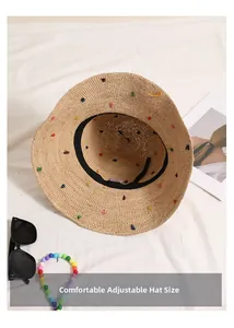 Détail d'un chapeau de soleil en paille beige avec pois colorés et bord réglable