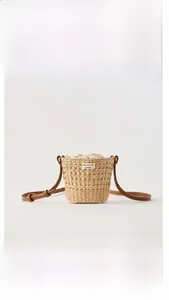 Détail d'un sac seau en paille tressée avec fermeture à cordon et bandoulière en cuir