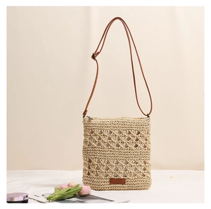 Close-up of bohemian hollow-out straw bag with brown leather strap and detail stitching