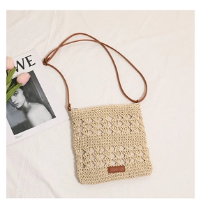 Detailed macro of hand-woven hollow pattern on straw crossbody bag with leather logo