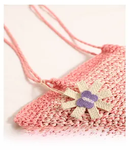 Close-up of pink woven straw bag featuring 3D floral accents and slender shoulder strap