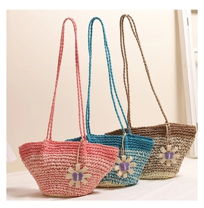 Detailed view of woven straw shoulder bags in pink, blue, and brown with floral charms