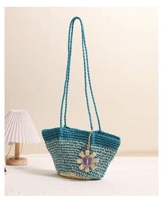 Detail of gradient blue woven straw beach bag featuring a floral charm and woven strap