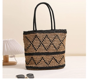 Detail of woven straw tote bag with black geometric patterns and round top handles