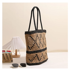 Detail of handwoven straw tote bag with black geometric lines and braided handles