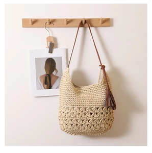 Detail of hollow woven straw shoulder bag featuring a brown leather strap and tassel