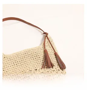 Detailed close-up of woven hollow pattern straw bag with brown leather strap and tassel