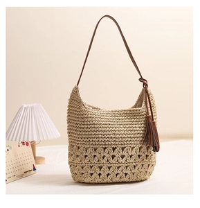 Detail of hollow woven straw bag with brown leather strap and stylish tassel pendant