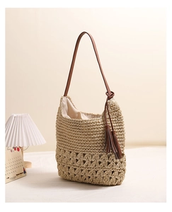 Detail of hollow-out handwoven straw tote bag with brown leather strap and stylish tassel