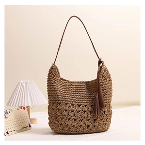 Detail of hollow-out straw shoulder bag featuring brown leather straps and twin tassels