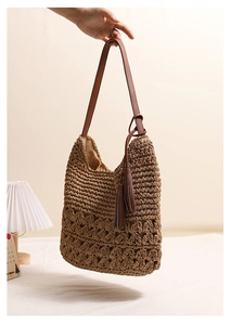 Close-up of bohemian hollow straw bag featuring tassels and brown leather shoulder strap