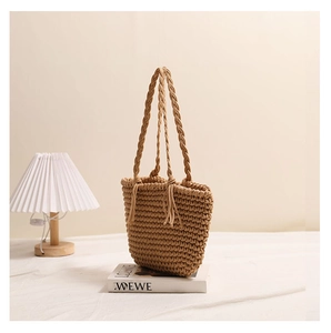 Detail of woven khaki tote bag with fringe accents on a cream background with soft lighting