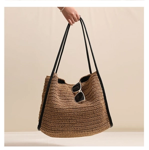 Dettaglio della borsa tote in paglia intrecciata con tracolla nera e occhiali da sole