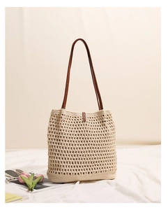 Detail of beige woven tote bag with brown leather straps on a soft fabric background