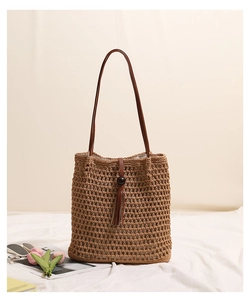 Close-up of woven straw tote bag featuring a leather tassel and round bead detail