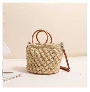 Détail d'un sac seau en crochet beige avec texture à pompons et poignées en bois rondes