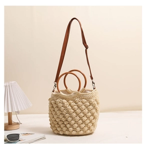 Détail de la texture tissée popcorn et des poignées rondes en bois d'un sac en paille