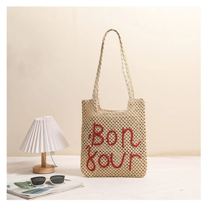 Detail of hollow straw tote bag featuring red Bonjour embroidery and handwoven texture