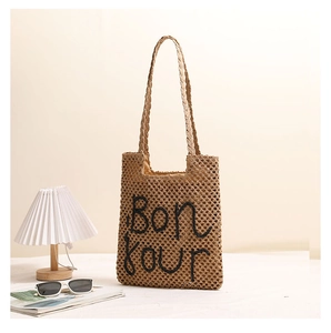 Detail of hand-woven straw shoulder bag featuring Bonjour embroidery for summer vacations