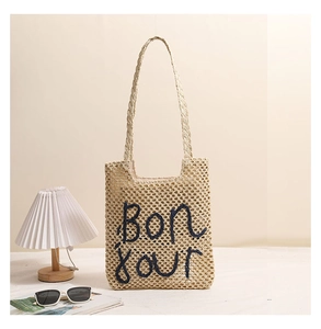 Detailed view of beige straw shoulder bag with blue Bonjour embroidery in a cozy setting