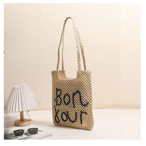 Detail of beige woven straw tote bag featuring black embroidered Bonjour lettering and handles