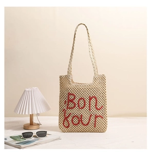 Close-up of Bonjour red embroidery on beige straw bag with hollow woven mesh detail
