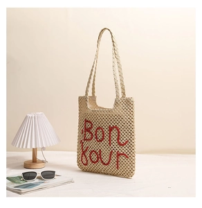 Detail of red Bonjour embroidery on a beige woven straw tote bag for beach vacation