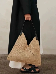 Macro shot of French triangle straw tote bag showing raffia weave and black leather handle
