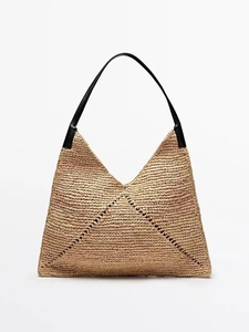 Detail of the raffia woven texture and black leather shoulder strap on the tote bag