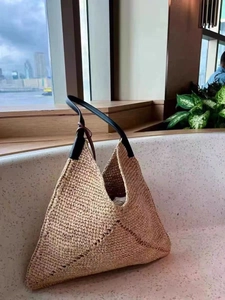 Close-up of woven straw texture and premium black leather strap on triangle tote bag