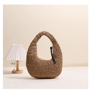 Detail of a brown woven straw handbag featuring a stylish black tassel and a semi-circular design