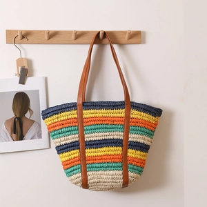 Colorful striped woven straw tote bag with brown leather straps hanging on a wooden rack
