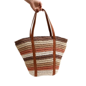 Striped straw tote bag with leather handles shown in hand for beach or summer vacation