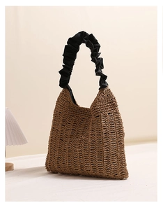 Detail of a brown woven straw tote bag featuring a black scrunchie handle for beach vacation