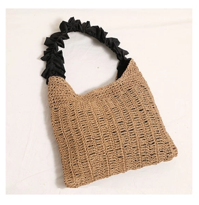 Detail of hand-woven straw tote bag featuring black ruffled fabric elastic handles