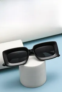 Detail of matte black rectangular sunglasses on a white pedestal with blue background