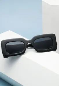 Close-up of black rectangular sunglasses on a white geometric stand with blue background