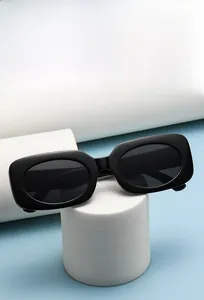 Detail view of rectangular black sunglasses on a white pedestal with soft blue background