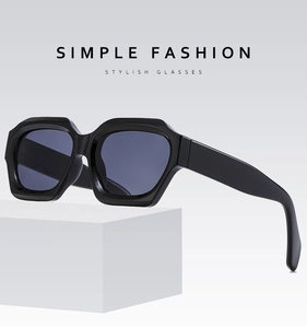 Detail of chunky black frame sunglasses with dark lenses on a minimalist white stand