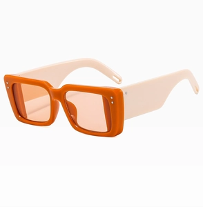 Detail view of rectangular orange sunglasses with cream wide temples and silver rivets
