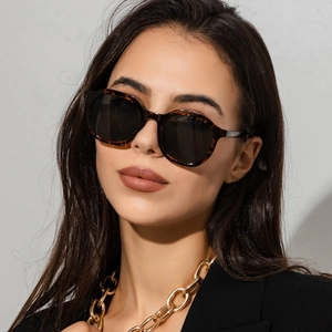 Close-up of tortoiseshell polygon sunglasses on model with a gold chain necklace