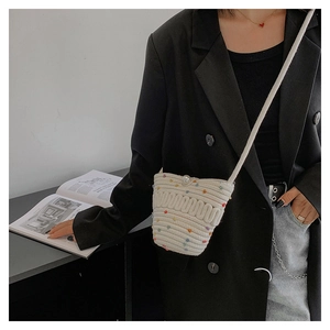 Detail of cream woven mini bag with colorful pom-poms and elegant pearl buckle closure
