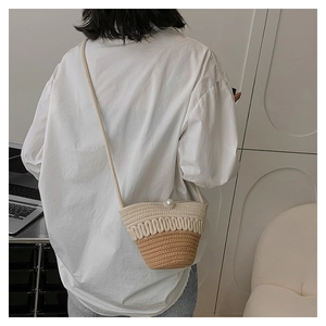 Detail of crossbody straw bucket bag with pearl clasp and shoulder strap on model